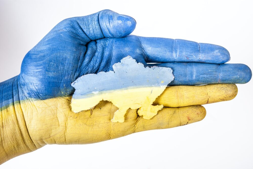 Innsida av ei hand måla som det ukrainske flagget, øvre del ljos blå og nedre del gul, oppå ligg eit ark med omrisset av Ukraina. Foto